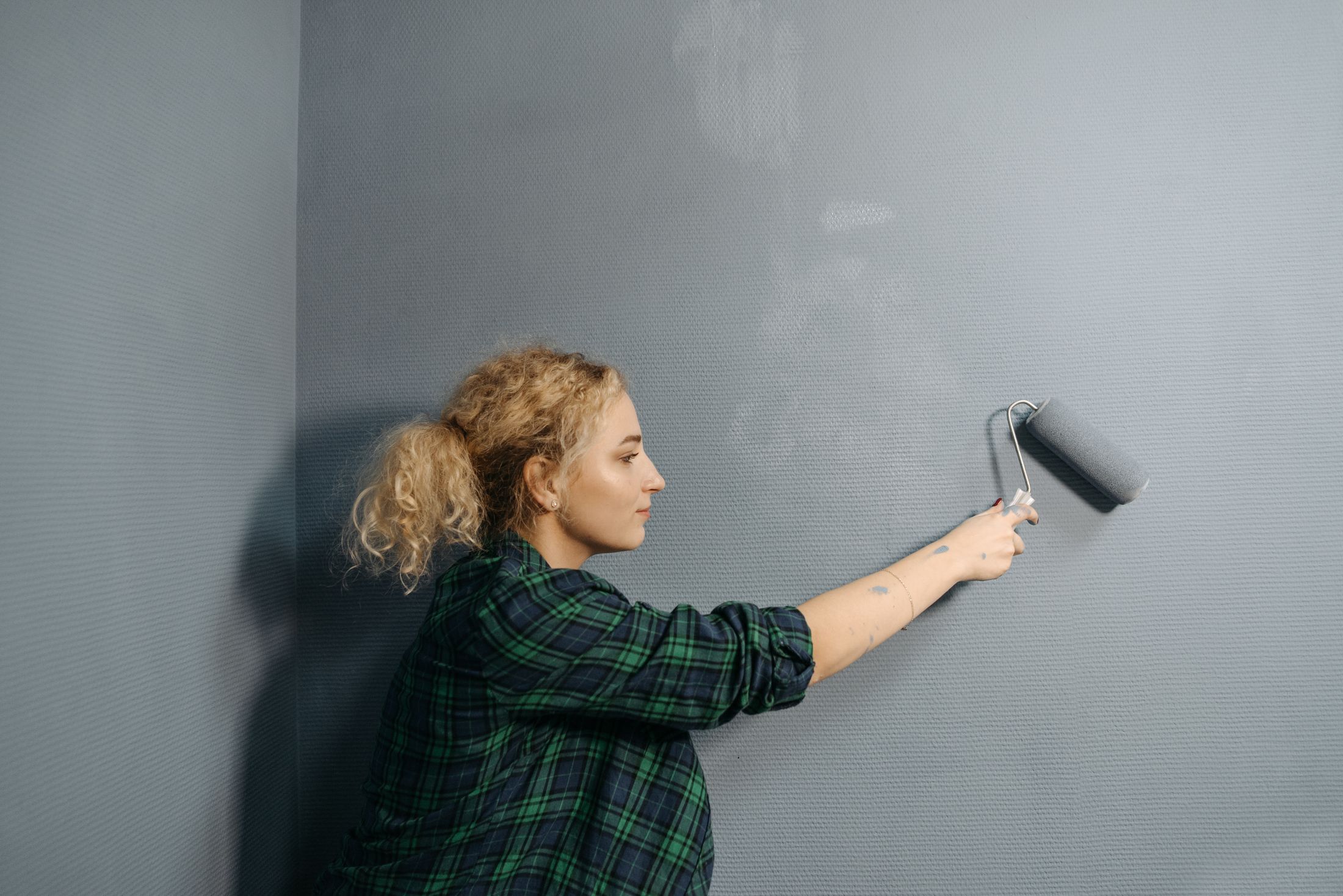 Professional painter rolling fresh blue-gray paint onto an interior wall